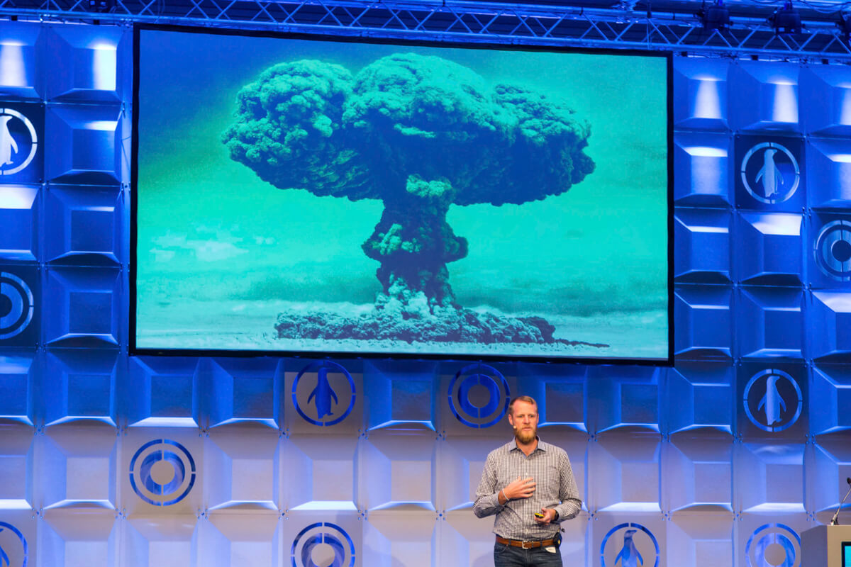 Rendezvényfotózás során készült kép egy eladóról, akinek a háta mögött egy atombomba kép van.